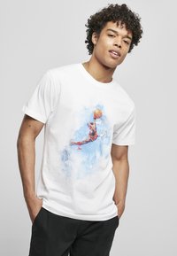 Hvid bomulds t-shirt med et farverigt grafisk design af en basketballspiller i luften, omkranset af blå akvarel-accenter.