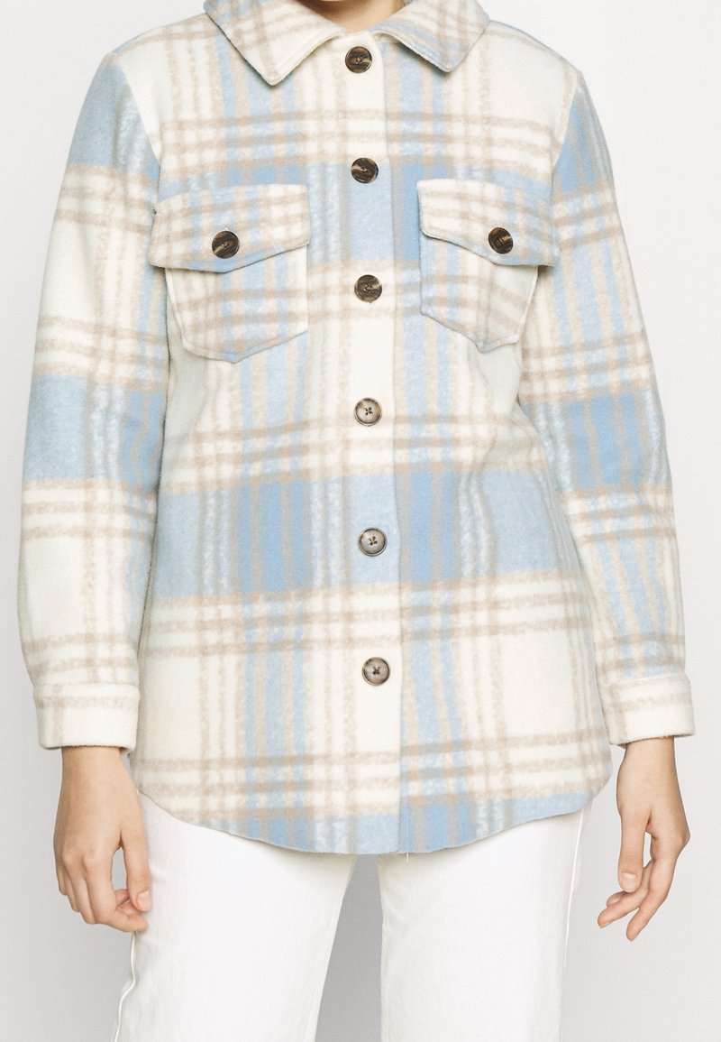 Geruite shirtjack in zachte, fluffy stof met blauwe, witte en beige kleuren. Beschikt over twee borstzakken en donkere knopen.