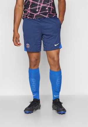 Marineblå sportshorts med blå accenter og Paris-logo; parret med knæhøje blå strømper og sorte gymsko med blå detaljer.