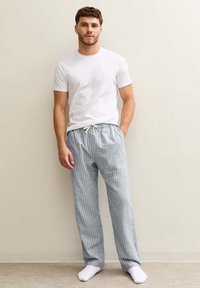 T-shirt blanc léger associé à un pantalon de pyjama à rayures bleues et blanches, doté d'une taille élastique et d'un cordon de serrage. Le mannequin se tient devant un fond neutre.