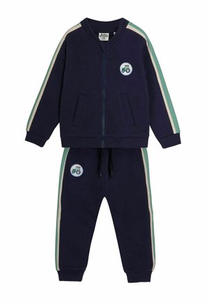 Mornarska trenerka z zadrgo in hlačami na elastiko. Ima zelene in smetane proge, dva žepa ter nalepko traktorja.