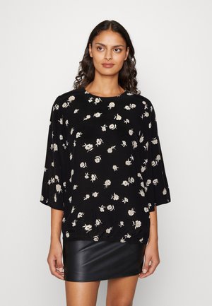 Μαύρη ανθισμένη μπλούζα με τρία τέταρτα μανίκια, με λευκά και μπεζ σχέδια λουλουδιών, ραμμένη λεπτομέρεια στο τελείωμα, συνδυασμένη με μια μαύρη δερμάτινη κοντή φούστα.