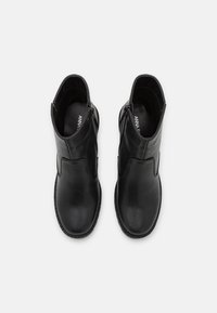 Par de botas de cuero negro hasta el tobillo con cremalleras laterales, punteras redondeadas y suelas planas, vistas desde arriba sobre un fondo blanco.