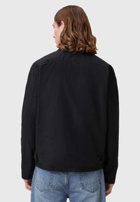Čierna ľahká bunda so striedmym strihom. Disponuje jednoduchým dizajnom, gombíkovými detailami a je kombinovaná so svetlými džínsami.