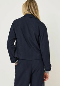 Navy pruhovaný zkrácený kabát s klopami a vyhrnutými rukávy, s jemnou texturou a minimalistickým designem.