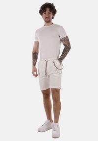 Camiseta blanca, pantalones cortos blancos con cintura elástica, acento de cordón y bolsillos. El modelo lleva zapatillas blancas. Fondo liso.