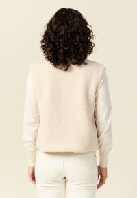 Fleece vest in lichtbeige, met een hoge kraag, zonder mouwen en een gestructureerd oppervlak, gecombineerd met lichtgekleurde broek.