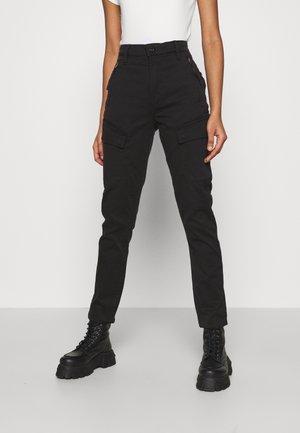 Black cargo pants with multiple side pockets, tapered fit, and a smooth cotton fabric. Worn with chunky black lace-up boots.