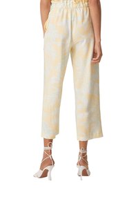 Pantalons courts jaune clair avec un motif de feuilles en vert menthe. Comprend une taille élastique et des poches latérales, associés à des talons hauts blancs.