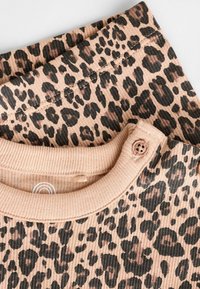 Leopardmönstrad skjorta med ribbad textur, med en ljusrosa bakgrund och svarta/bruna fläckar, samt en knäppt halsringning.