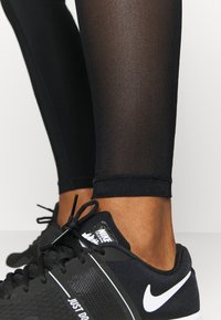 Czarne legginsy z przezroczystym panelowym wstawieniem, o dopasowanym kroju. Zestawione z czarnymi trampkami z białym logo Nike i sznurowadłami.