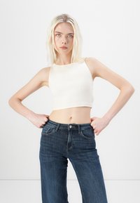 Kremast ribana crop top z okroglim izrezom, v kombinaciji z visokim pasom modrimi kavbojkami, ki imajo klasičen dizajn s petimi žepi.