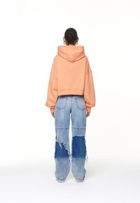 Felpa corta color pesca con cappuccio, abbinata a jeans azzurri chiari con orli sfrangiati e una sfumatura di colore che va dall'azzurro chiaro a quello scuro.