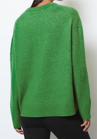 Vihreä neulottu villapaita, jossa on rento istuvuus, pyöreä kaula-aukko ja ribbaushelma. Ominaisuuksiin kuuluu teksturoitu pinta ja pudotettu olkalinja mukavuutta varten.