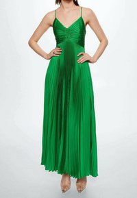 Robe plissée verte avec un corsage ajusté et des bretelles fines, s'étendant en une jupe longue jusqu'au sol. Tissu lisse et brillant avec des plis verticaux.