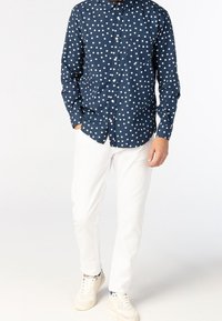 Camicia blu con bottoni, decorata con pois bianchi, abbinata a pantaloni bianchi e sneaker chiare. La camicia ha colletto e maniche lunghe.