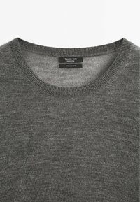 Grauer Kaschmirpullover mit Rundhalsausschnitt. Weiche Textur und glatte Strickart. Pflegeetikett sichtbar, das 100 % Kaschmirmaterial angibt.