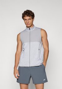 Sleeveless, light gray vest with a high collar, zip closure, and side pockets; features a textured fabric and subtle branding accents.