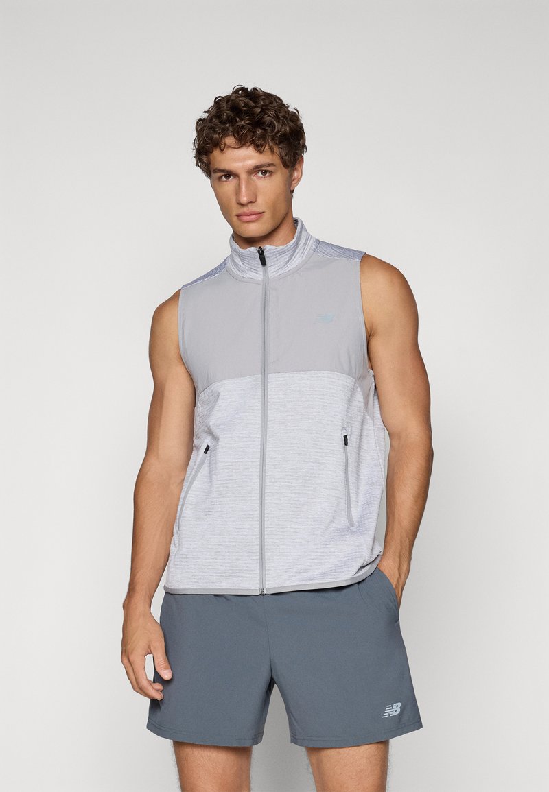 Sleeveless, light gray vest with a high collar, zip closure, and side pockets; features a textured fabric and subtle branding accents.