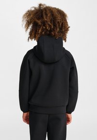 Svart huvtröja med avslappnad passform, med ribbade ärmslut och nederkant, tillverkad av mjukt material med en slät yta.