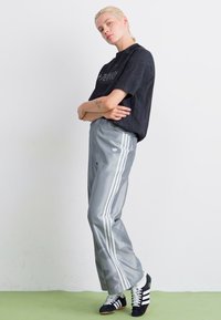 Zwarte oversized t-shirt, grijze trainingsbroek met witte strepen en zwarte sneakers. De outfit heeft een loose fit en een minimalistisch ontwerp.