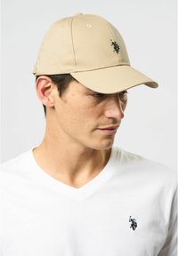Khaki baseball cap with a curved brim, featuring a black embroidered logo on the front. Made of durable, textured fabric.