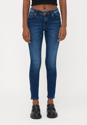 Tanke jeans v temno modrem denimu. Imajo sprednje žepke, pasne zanke in majhen zavihek pri gležnju. Trden material z gladko teksturo.