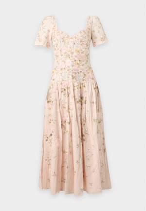 Femme portant une robe midi fleurie rose pâle avec des manches ballon et un décolleté en cœur, debout les mains dans le dos.