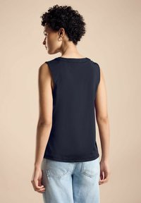 Svart ärmlös blus med en mjuk textur, rund halsringning och subtila stygn detaljer. Bärs med ljusblå högmidjade jeans.