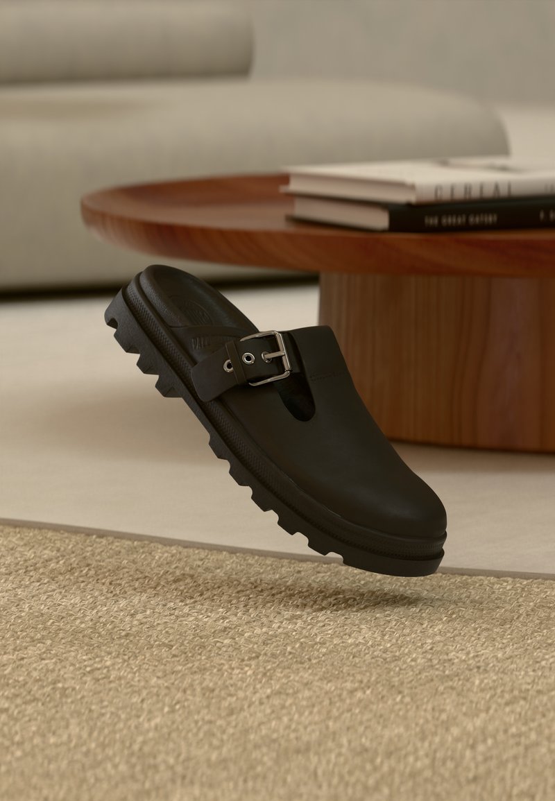 Μαύρο παπούτσι τύπου slip-on με φαρδιά μπροστινή άνοιξη, ρυθμιζόμενο ασημένιο αγκράφα, υπερμεγέλης λαστιχένια σόλα με βαθιές τάπες και λεία υφή.