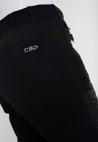 Gros plan d'un pantalon softshell noir avec une ceinture élastique, une poche latérale zippée et un logo blanc CMP sur la hanche arrière.