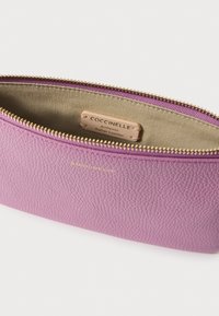 Rózsaszín bőr tároló tasak, texturált felülettel, arany színű cipzárral és bézs belső béléssel. Felirata: "Coccinelle Authentic Italian Leather".