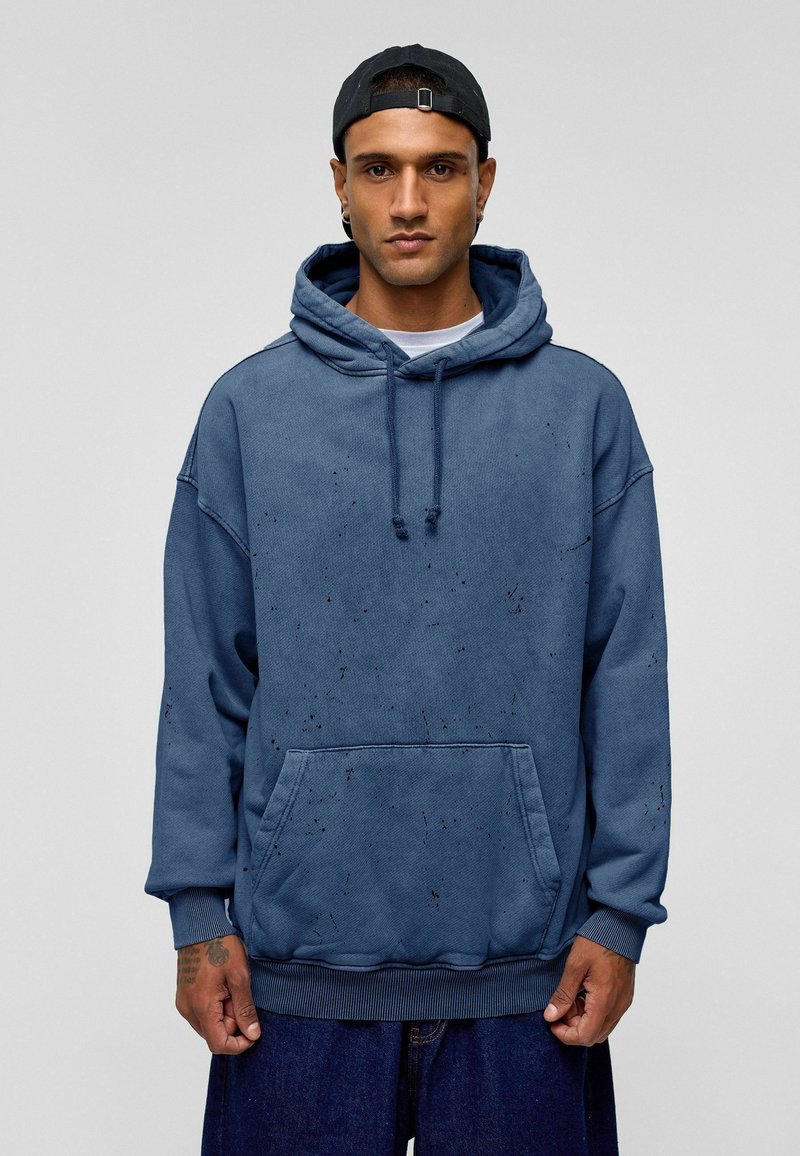 Blauwe oversized hoodie met een voorzak, trekkoorden en een textuur met vage spikkels. Gemaakt van een zachte, duurzame stof.