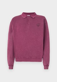 Pull en coton violet foncé avec un col et des poignets côtelés. Présente un petit logo sombre sur la poitrine gauche. Tissu doux et texturé.