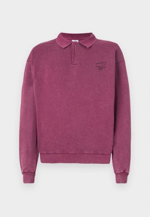 Pull en coton violet foncé avec un col et des poignets côtelés. Présente un petit logo sombre sur la poitrine gauche. Tissu doux et texturé.