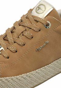 Baskets beiges en cuir synthétique texturé, avec une semelle espadrille tissée beige, des coutures blanches contrastantes et un accent de logo métallique.