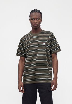 Jeune homme aux cheveux tressés portant un t-shirt à manches courtes rayé vert et blanc et un pantalon noir sur un fond uni.