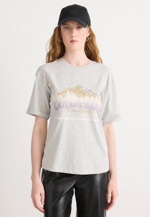 T-shirt grigio a maniche corte con grafica di montagne del Colorado in colori pastello. Abbinato a pantaloni in pelle nera lucida e un cappellino nero.