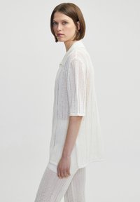 Wit gebreid shirt met korte mouwen en een polo-kraag, met een losse pasvorm, open geweven textuur en een rechte onderrand.