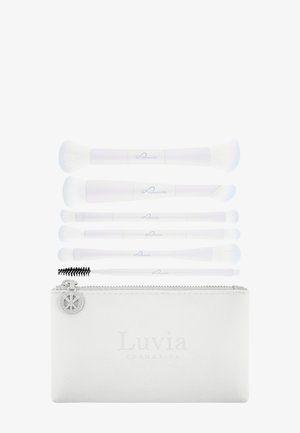 Ensemble de six pinceaux de maquillage blancs avec des poils blancs et une brosse spoolie, disposés au-dessus d'une pochette zippée blanche avec le logo "Luvia".