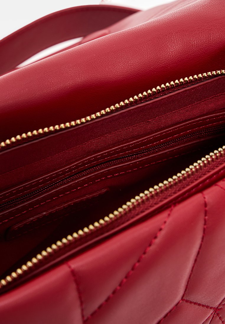 Interior de bolso de cuero acolchado rojo con bolsillos con cremallera dorados y forro suave. Diseño compartimentado para un almacenamiento organizado.