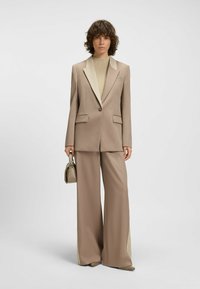 Beige suit featuring a tailored blazer with a contrasting collar, wide-leg trousers, and a textured knit top. Complements with a small handbag.