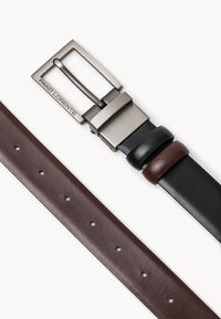 Odwracalny skórzany pasek z matową srebrną klamrą z wygrawerowanym logo. Jedna strona jest ciemno-brązowa, a druga czarna.