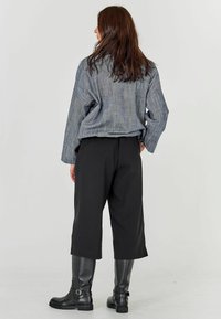 Liialt hallist triibulisest pikast varrukast särgist, mustadest laiast seelikutest ja põlvikudest kõrgematest mustadest nahknõudest, vaadates seljaga.