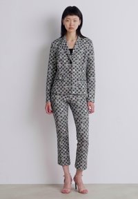 Gemusterter Anzug mit taillierter Blazerjacke und schmal zulaufenden Hosen, die Rautenmuster in Grau, Schwarz und Weiß aufweisen. Glattes Material, dezenter Glanz.