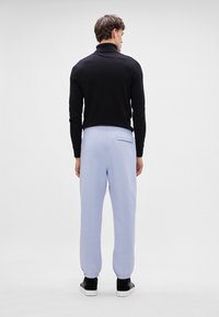 Μαύρο πουλόβερ με ψηλό λαιμό, ανοιχτό μπλε φόρμες με ελαστικές μανσέτες και πίσω τσέπη, σε συνδυασμό με μαύρα sneakers. Ουδέτερο φόντο.