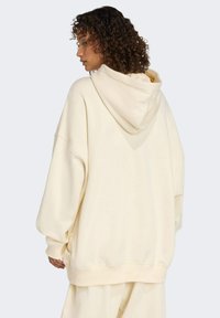 Krémová mikina s kapucňou s uvoľneným strihom, spadnutými ramenami a rebrovanými manžetami. Mäkká textúra s hladkým povrchom.