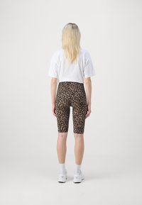 T-shirt bianco abbinato a pantaloni corti a stampa leopardata, con una texture liscia e lunghezza fino a metà coscia. Indossato con sneakers bianche.