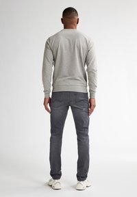 Sudadera gris con cuello redondo y puños acanalados, combinada con jeans gris oscuro y zapatillas blancas, vista desde atrás.