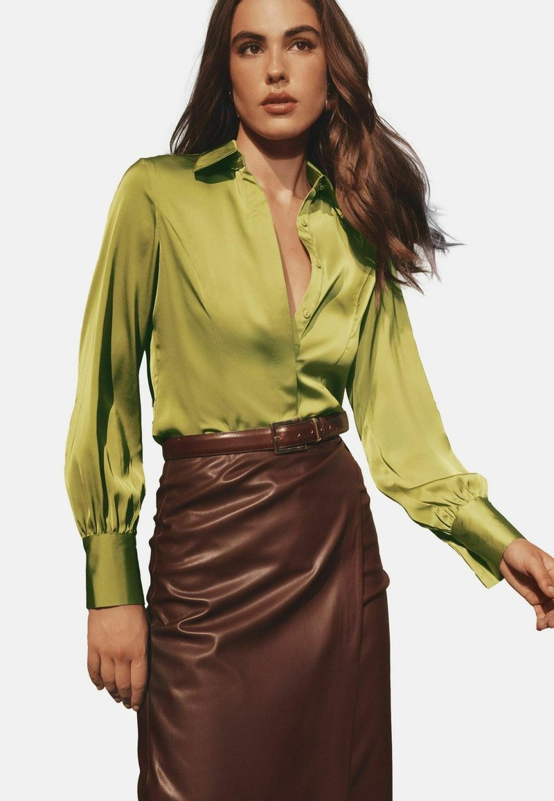Green satin blouse with a collared neck and puffed long sleeves, paired with a brown leather pencil skirt featuring a belted waist.